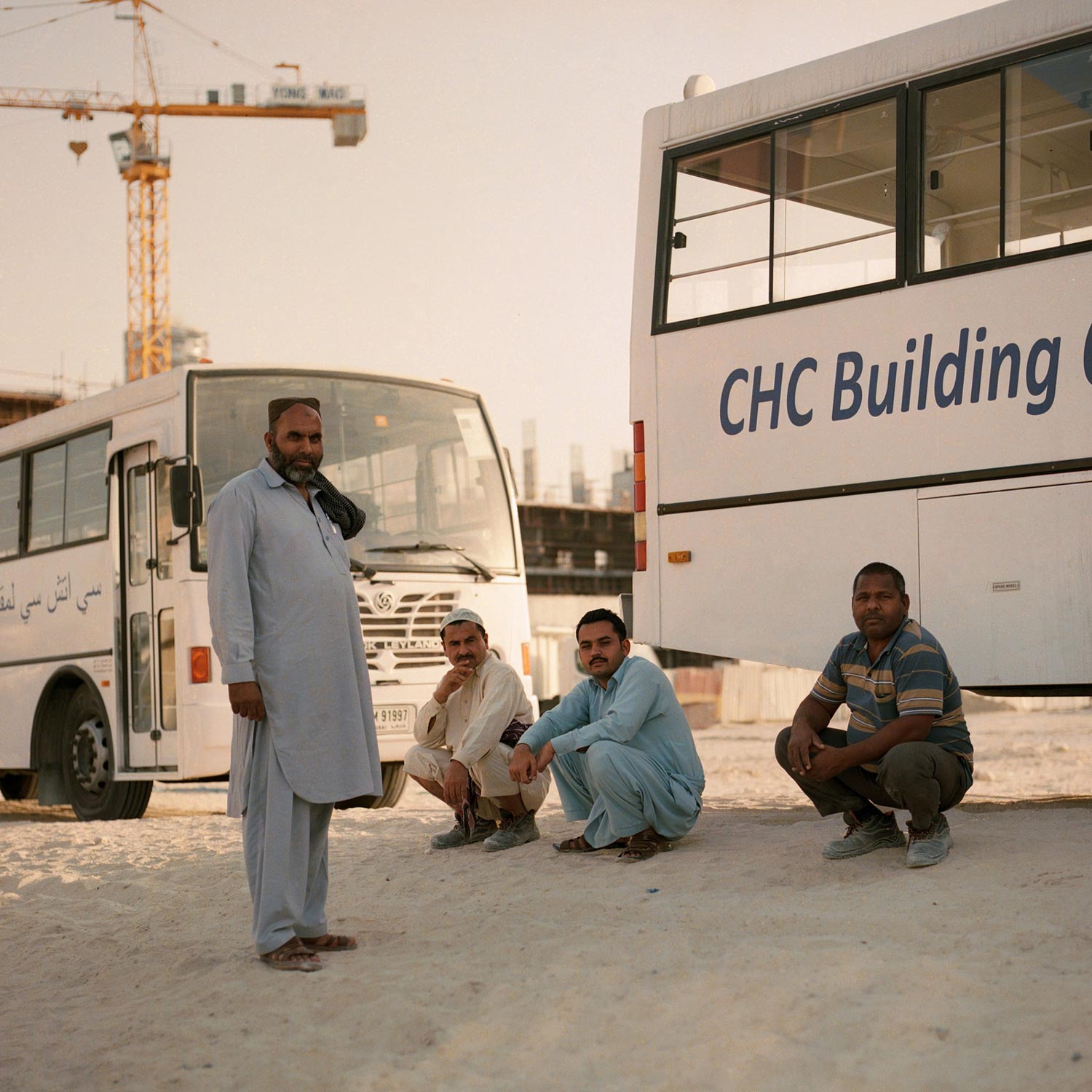 Indian construction workers sitting in the sand, waiting for a bus.