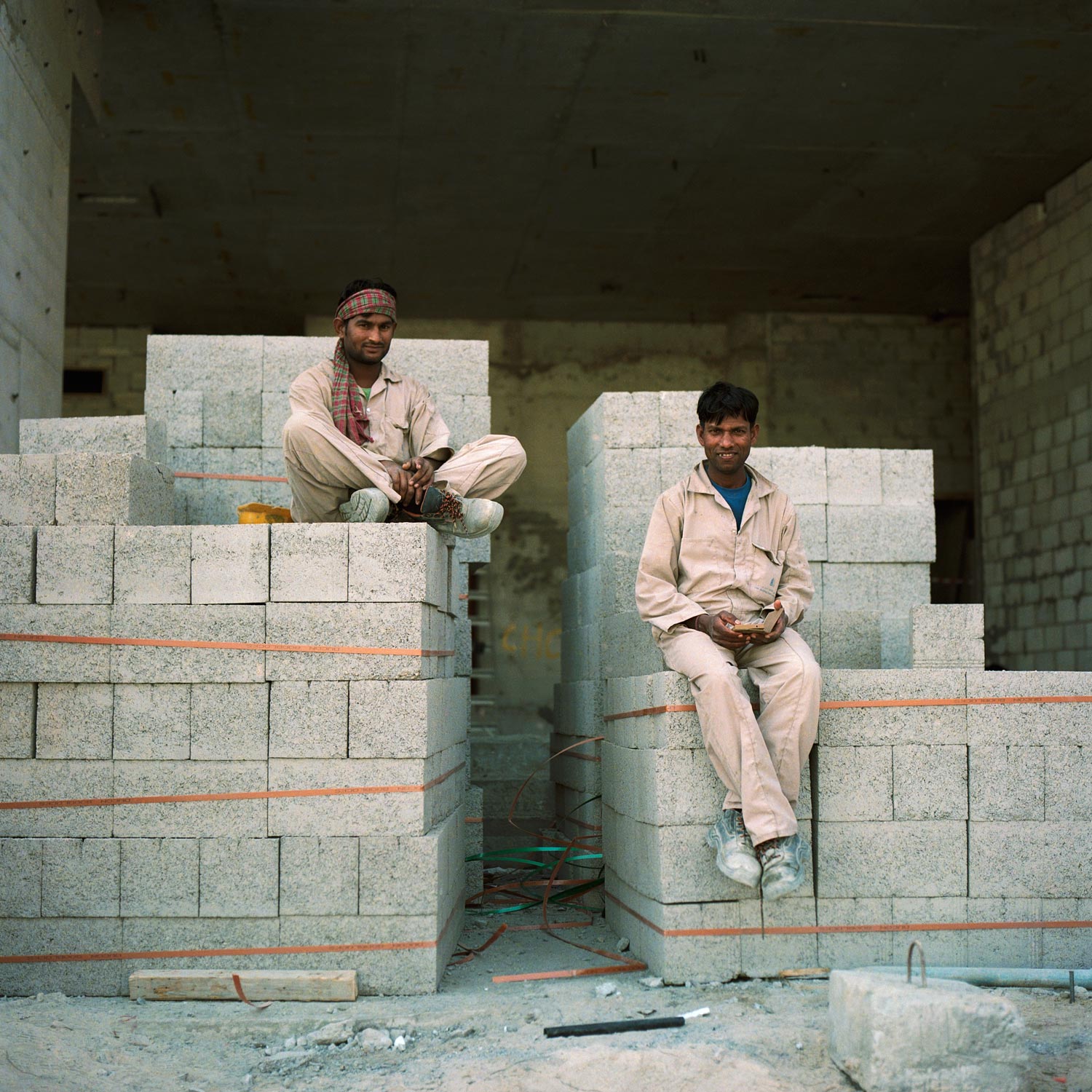 Two indian construction workers on a lunch break, sitting on a pile of concrete blocks in Dubai, Analogue photography.