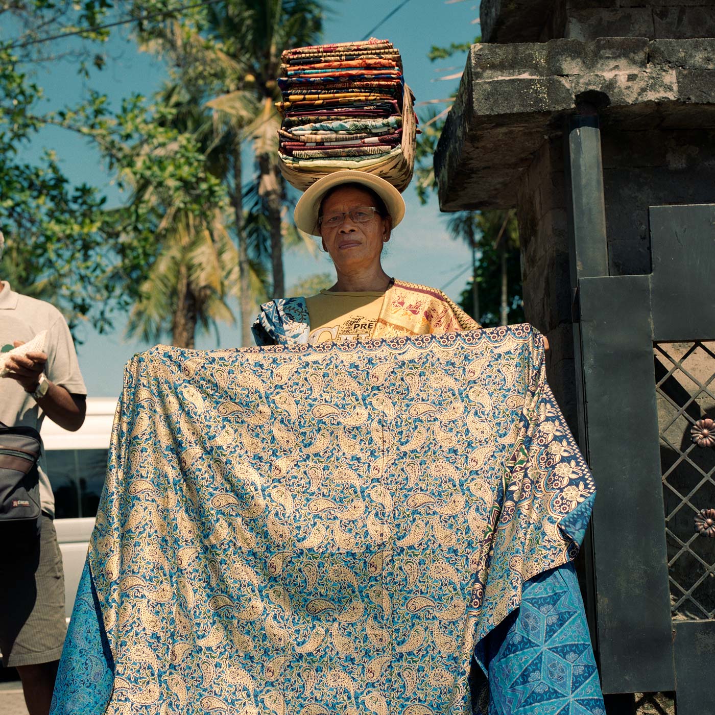 Female street trader selling Batik fabric wraps, with a pile of fabrics on her head.