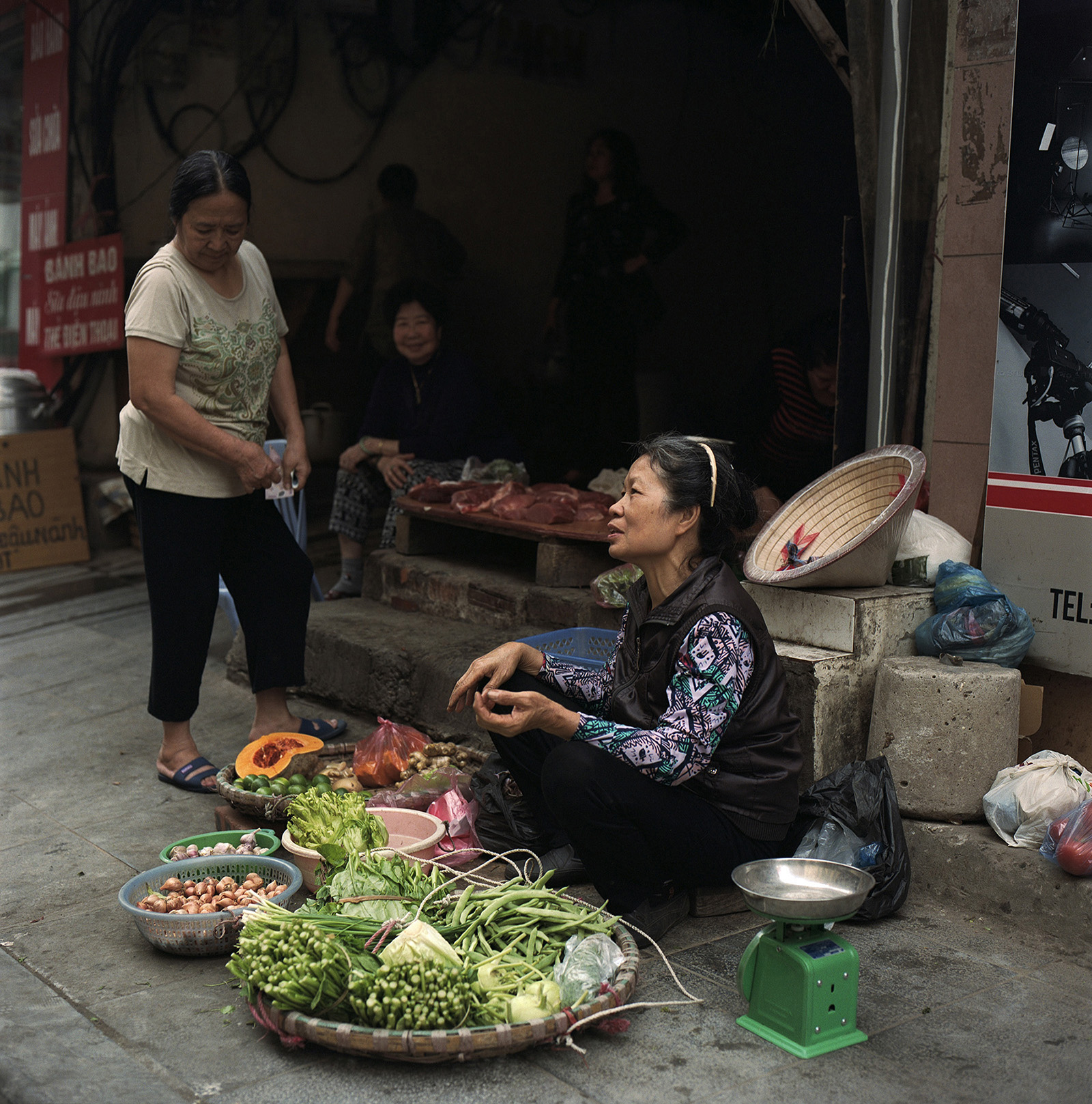 Female street trader selling fresh vegitables with other female traders. Streets of Hanoi, Vietnam