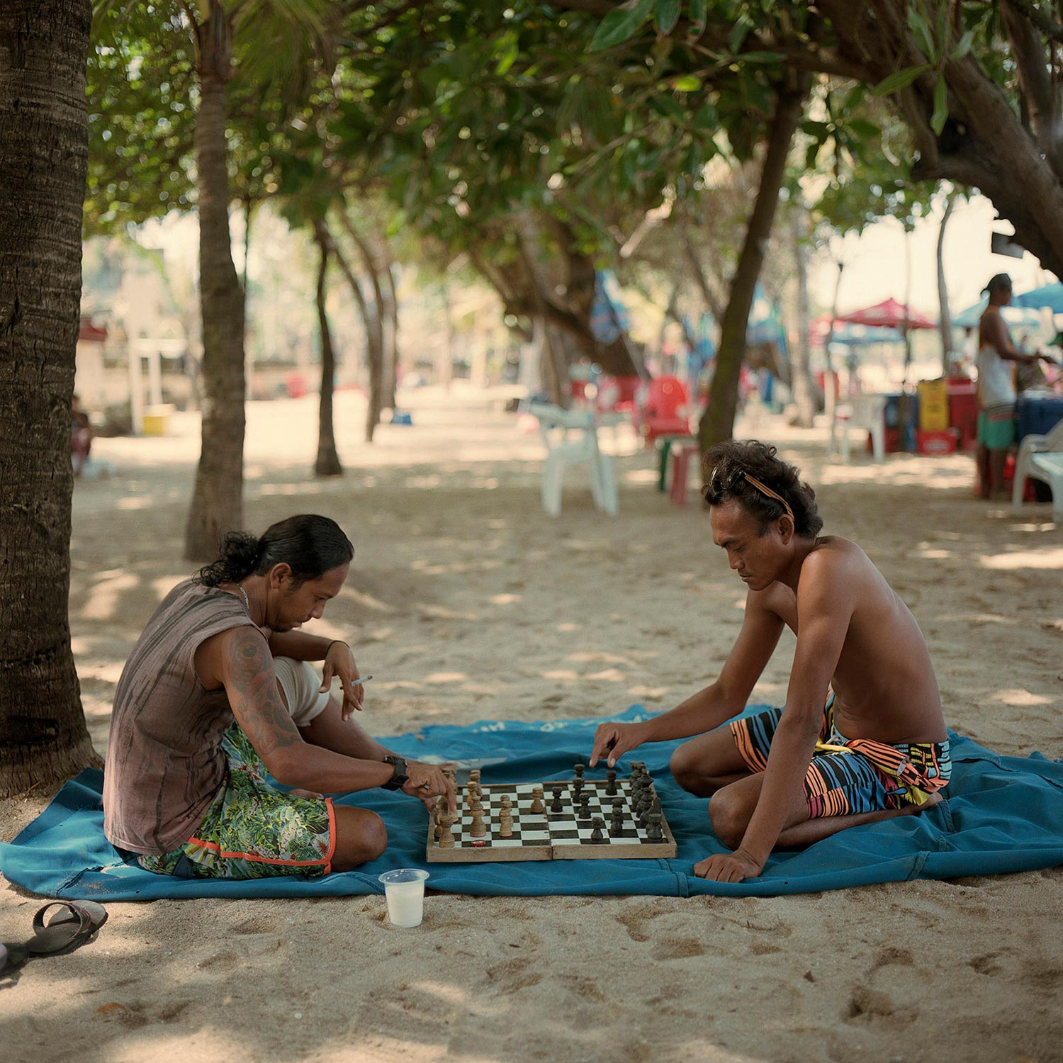 Two friends playing a game of chess ont he beach.