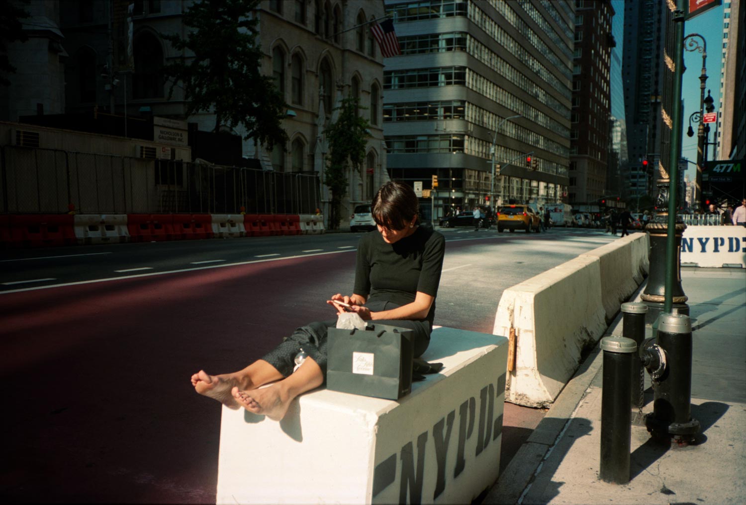 Woman taking a break, seated on a NYPD bollard, Manhattan street scenes.