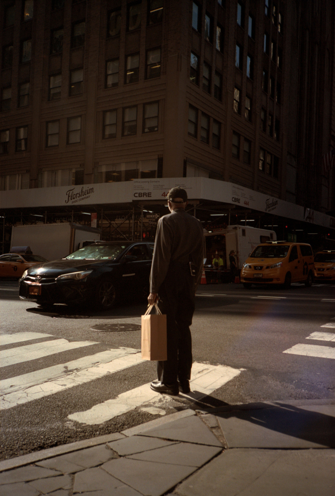 Man standing with brown paper bag at a crosswalk in Manhattan.