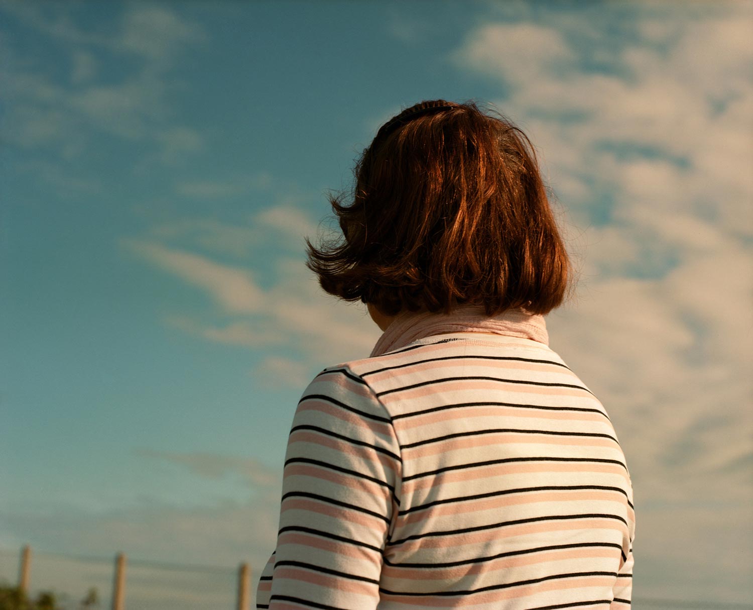 red haired woman from behind, looking at the clouds, analogue photography.