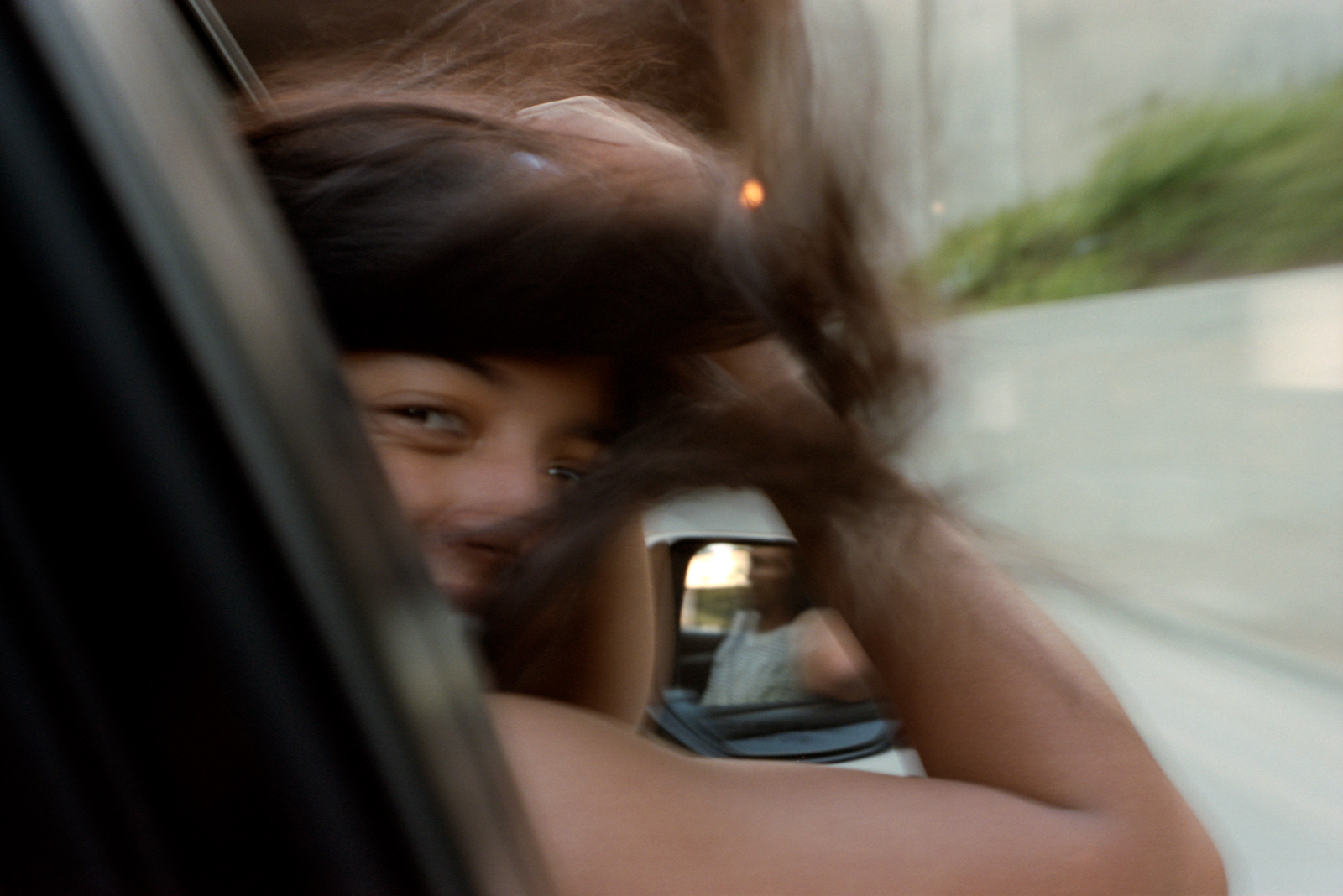 Playful young woman hanging out of car window, roadtrip in Los Angeles.